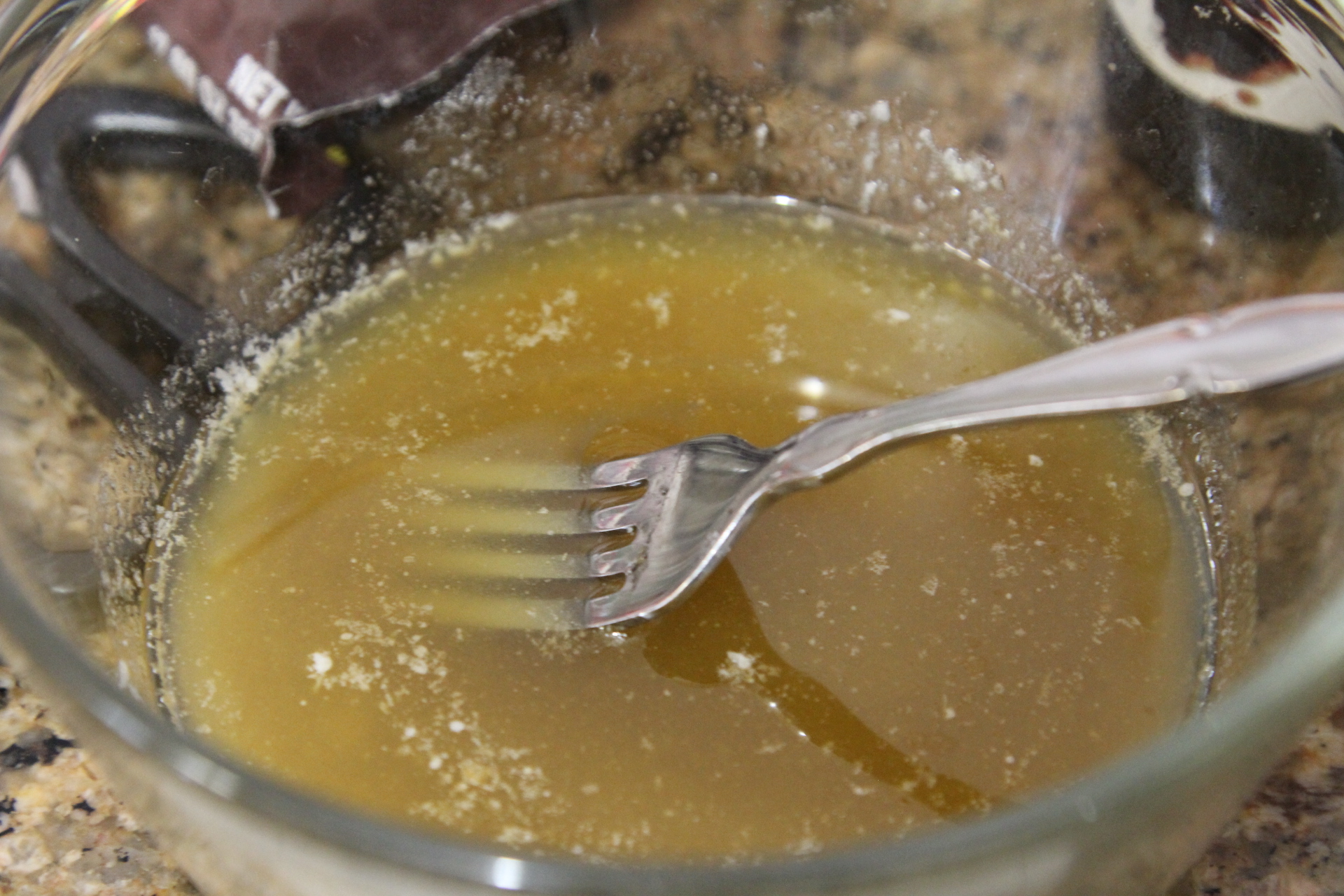 A small bowl of melted butter mixed with Worcestershire sauce and spices, with a whisk resting inside on a kitchen counter