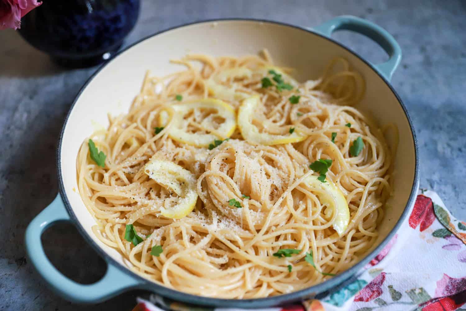 A small bowl of minced garlic next to cubes of butter and a lemon on a cutting board beside a skillet