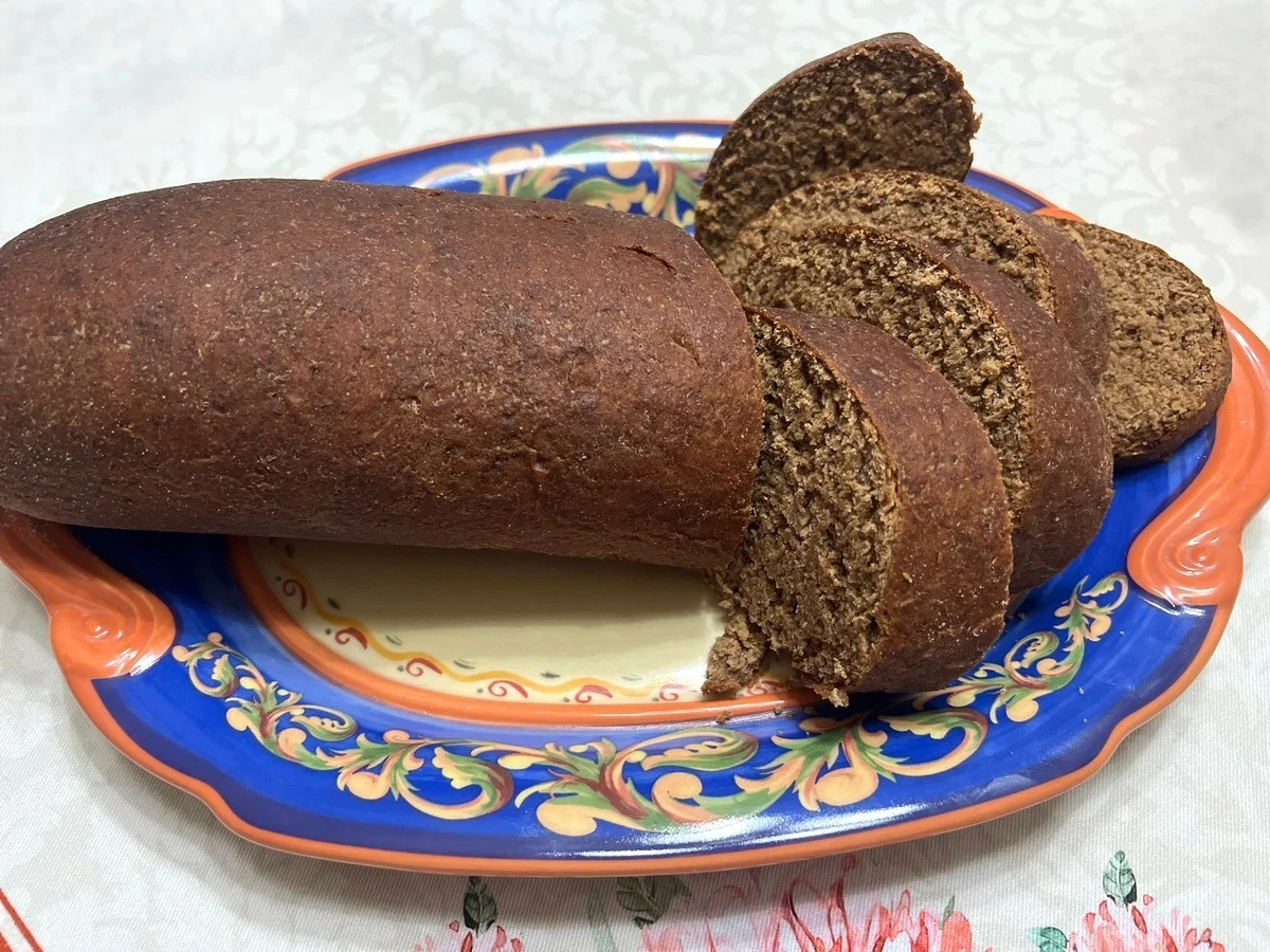 A small bowl of molasses next to cocoa powder and rye flour on a stone countertop with measuring spoons