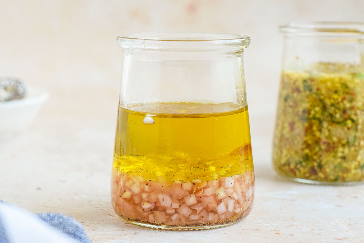 A small bowl of oil and vinegar dressing with oregano and black pepper on a kitchen counter next to a whisk