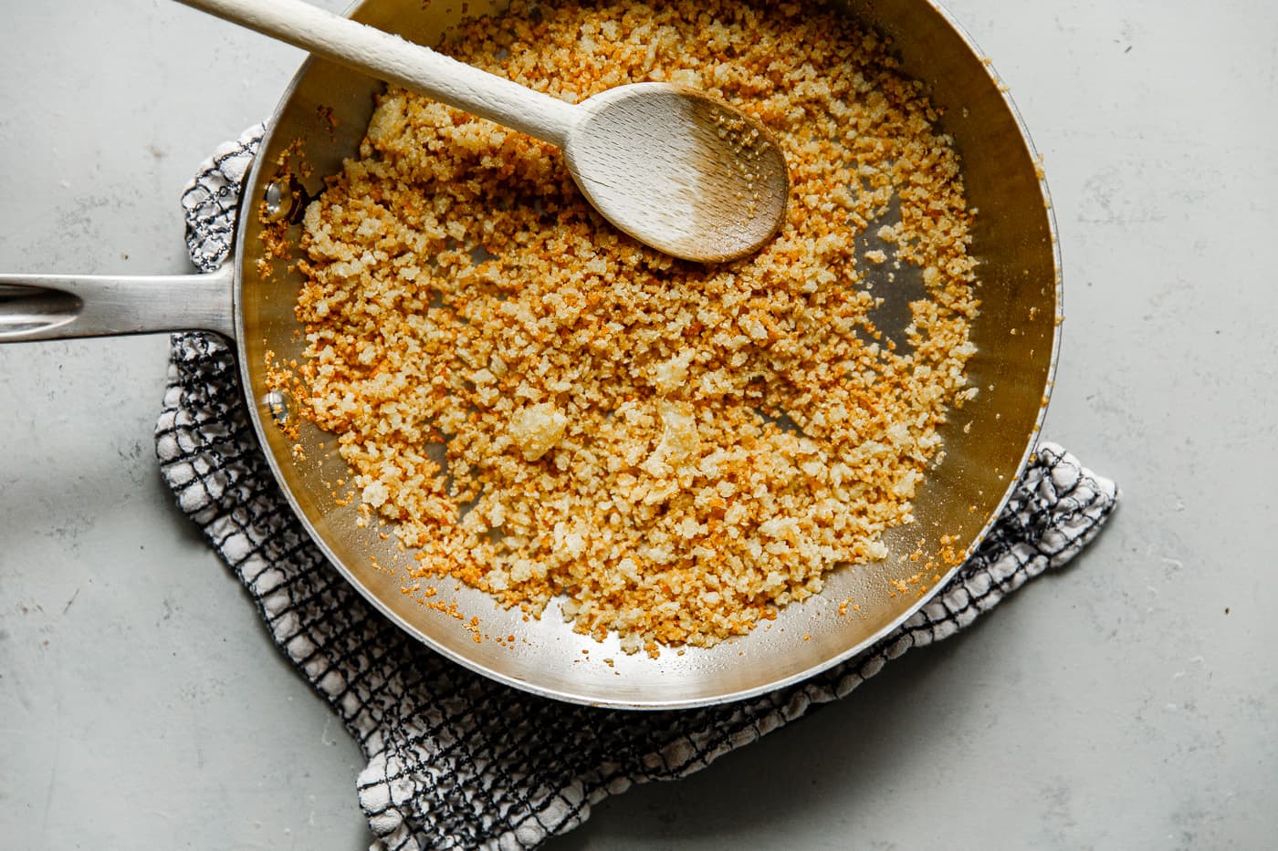 A small bowl of panko breadcrumbs with minced garlic and chopped parsley on a kitchen counter next to a lemon and a jar of olive oil