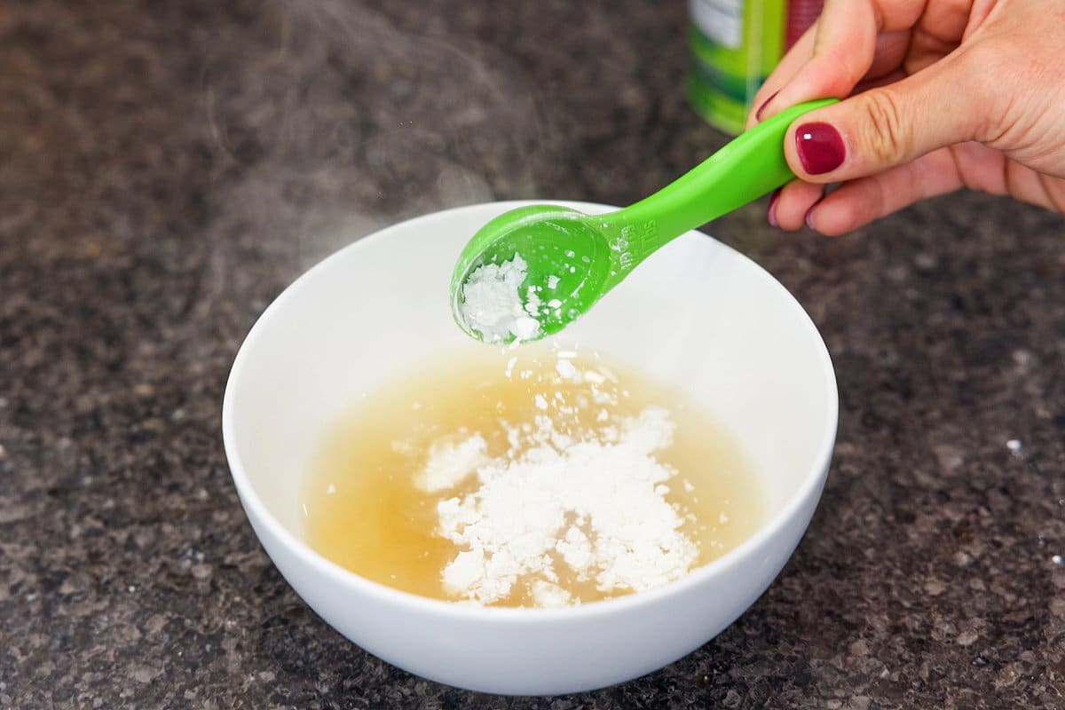 A small bowl of smooth cornstarch slurry with a spoon resting beside it on a clean kitchen counter
