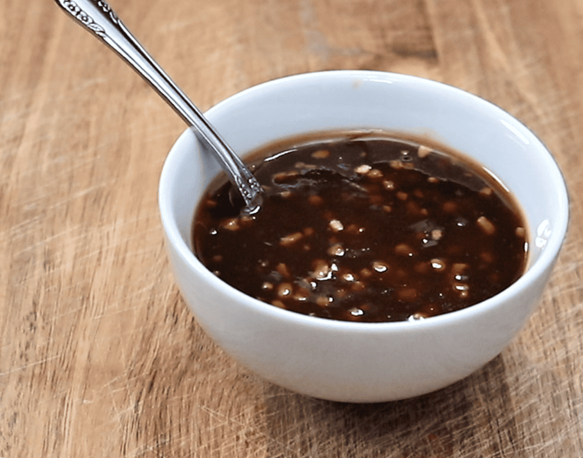 A small bowl of soy ginger stir fry sauce being whisked on a kitchen counter next to minced garlic and grated ginger