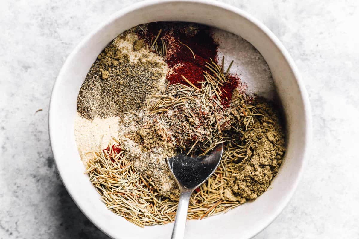 A small bowl of turkey dry rub being mixed with a fork on a kitchen counter, with spice jars nearby