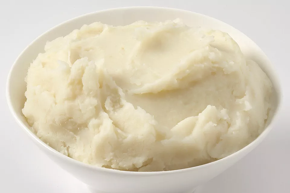 A small bowl of very smooth plain mashed potato with a spoon on a neutral kitchen counter
