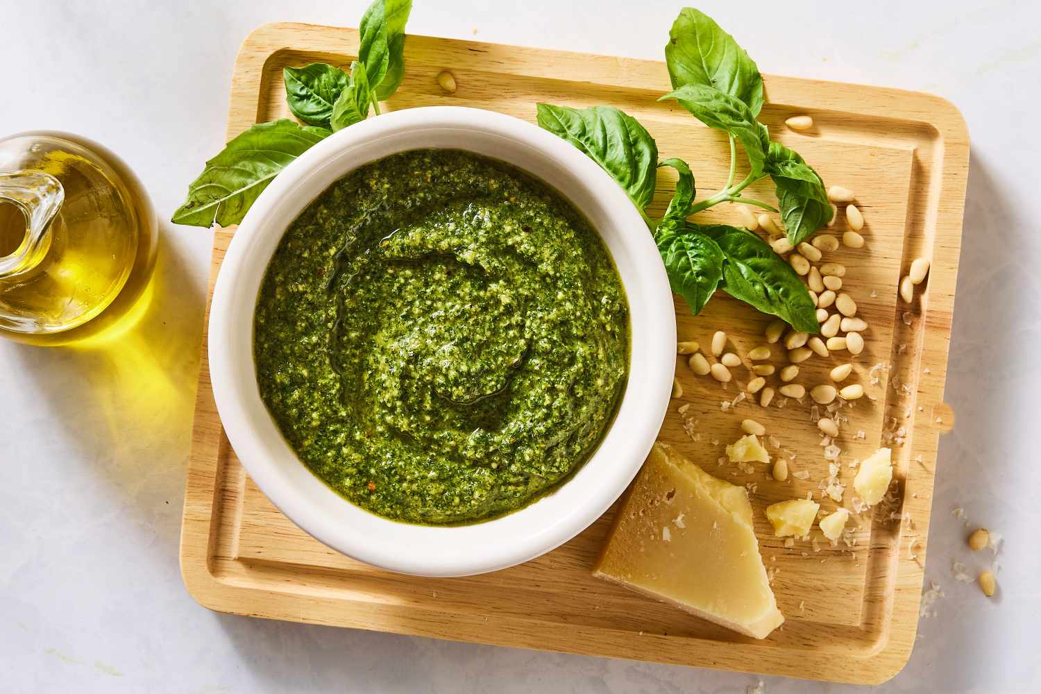A small bowl of vibrant green basil pesto sauce on a wooden counter with a spoon beside it