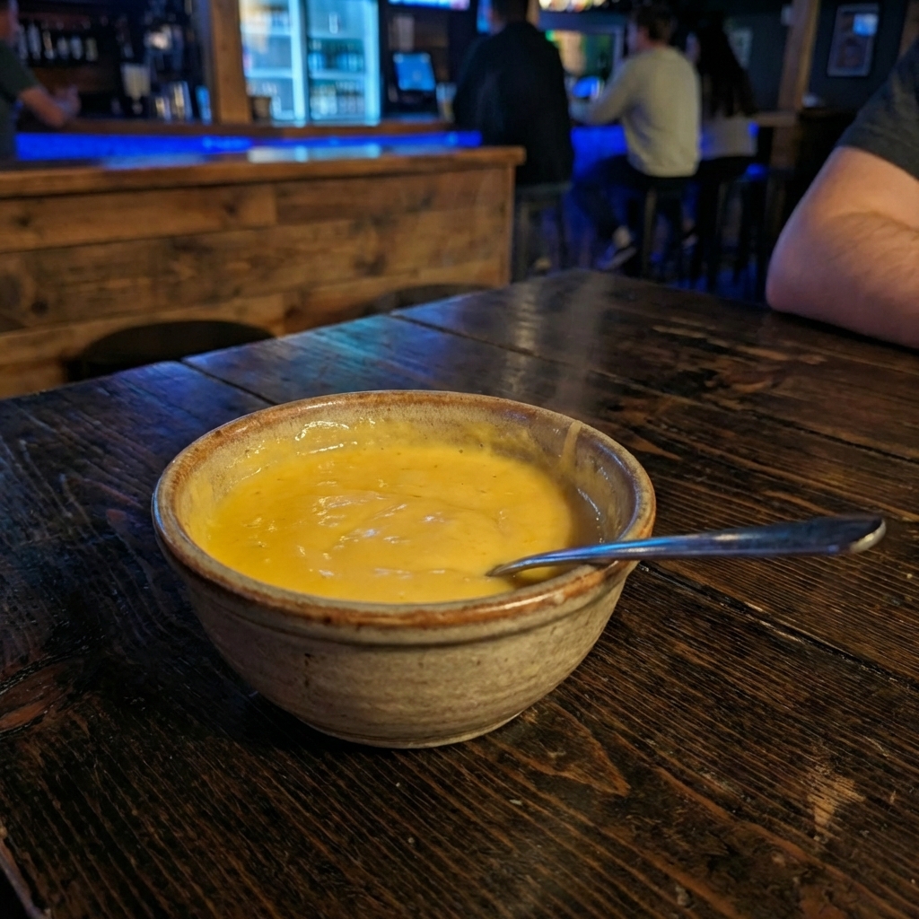 A small bowl of warm cheese sauce with a spoon beside it on a countertop