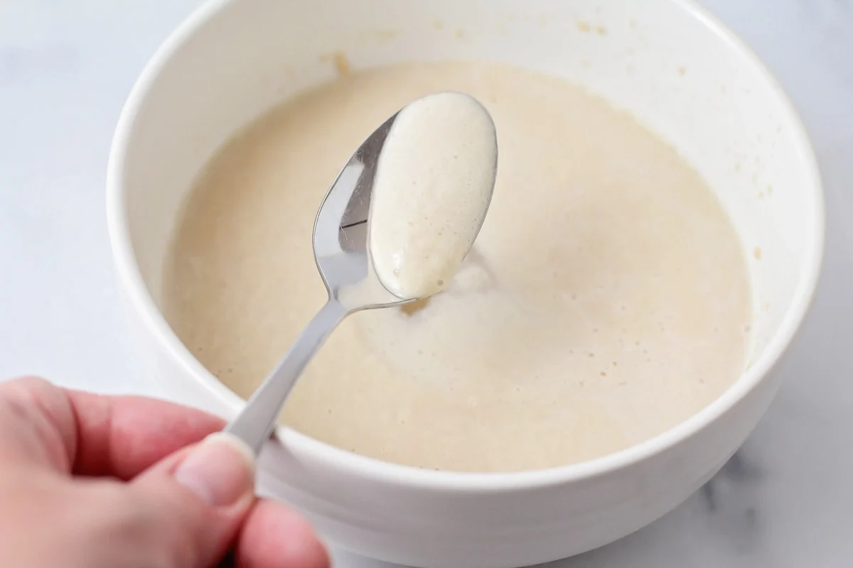 A small bowl of warm milk with yeast and sugar blooming on the surface, sitting on a kitchen counter