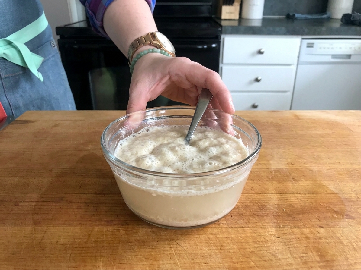 A small bowl of warm water with yeast and sugar blooming on the surface, foamy and active