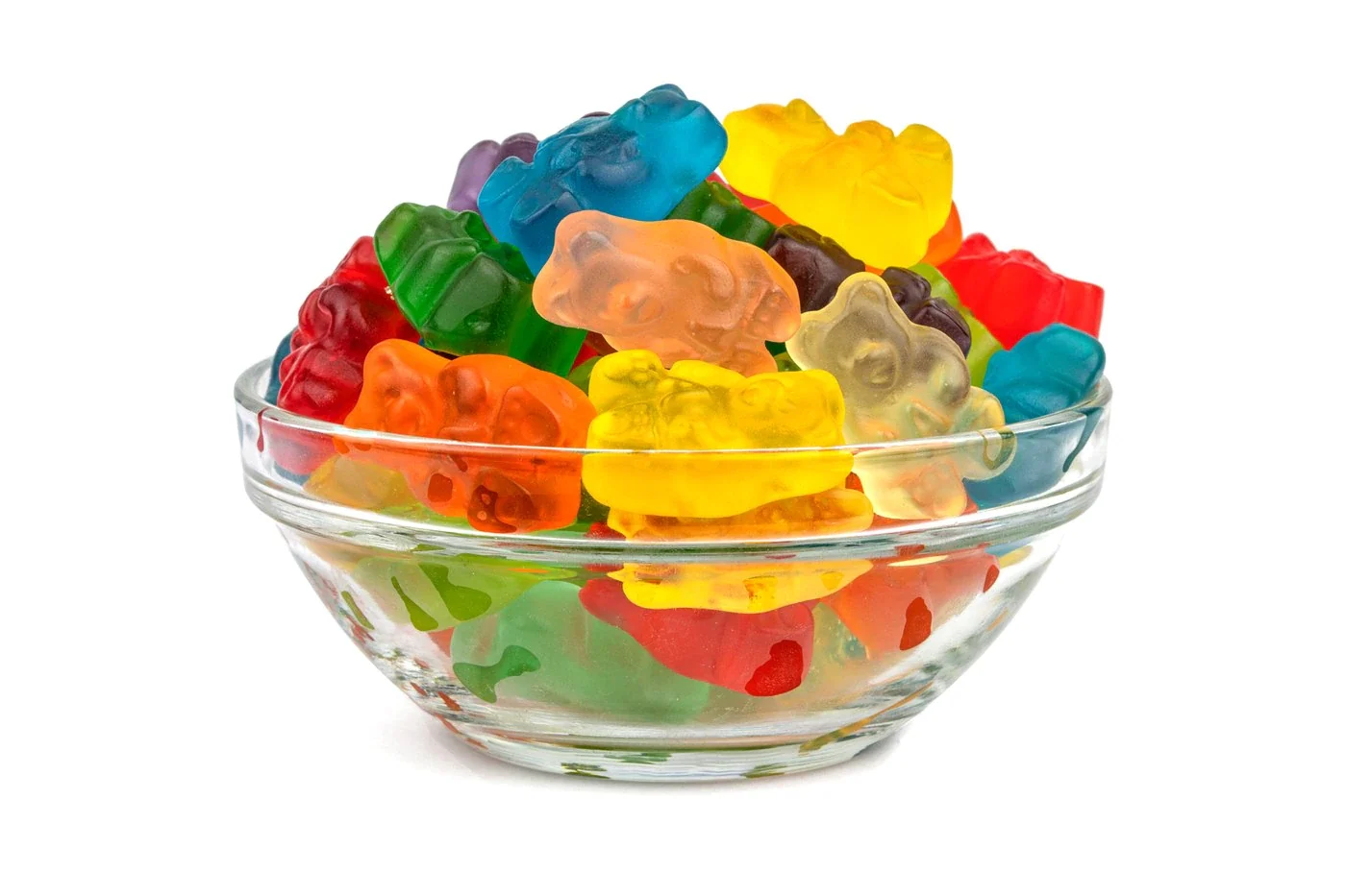 A small bowl overflowing with colorful gummy bears on a kitchen counter beside empty shot glasses and a cocktail shaker