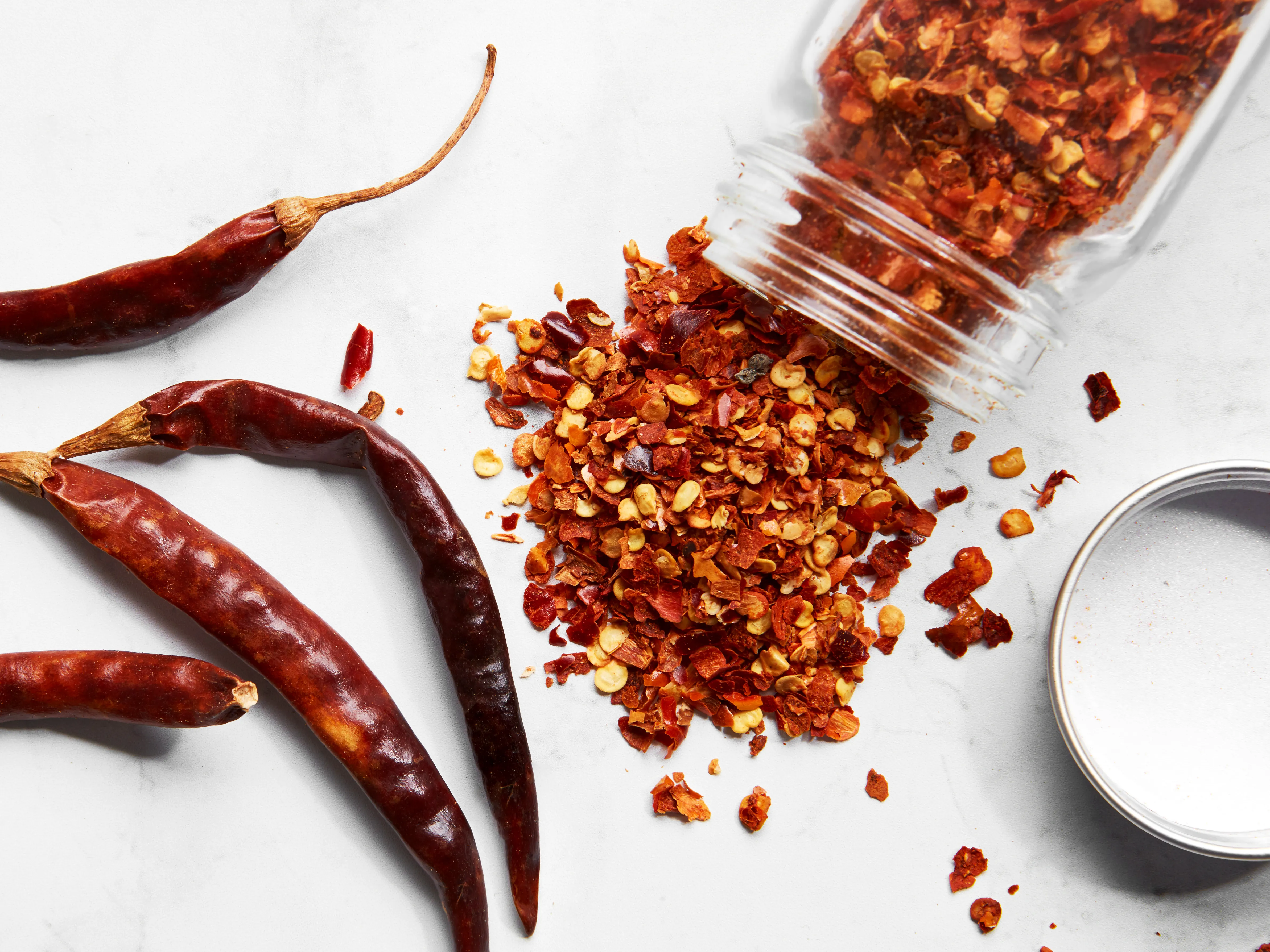 A small ceramic bowl filled with crushed red pepper flakes on a kitchen counter next to measuring spoons