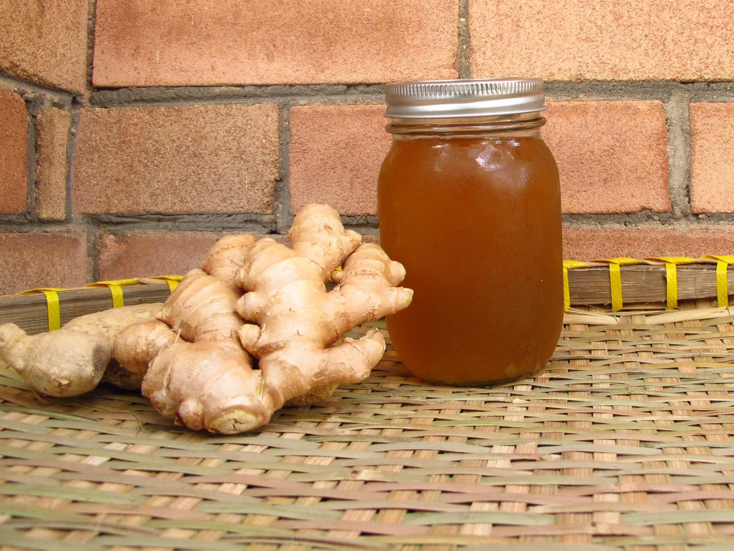 A small glass bottle of homemade ginger syrup on a light kitchen counter beside sliced fresh ginger and a lemon, warm natural light