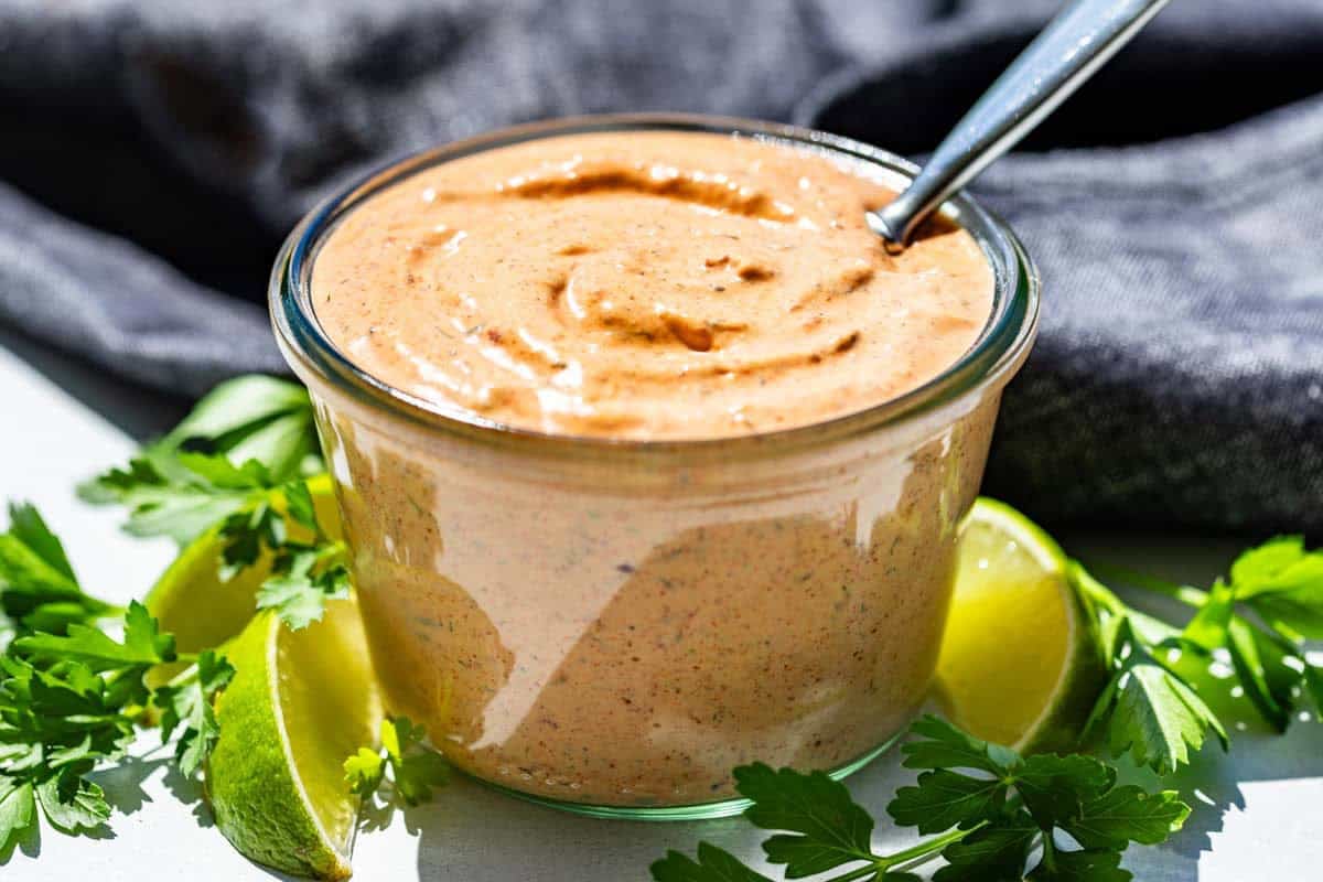 A small glass jar filled with chipotle aioli on a kitchen counter with a spoon dipped into the sauce