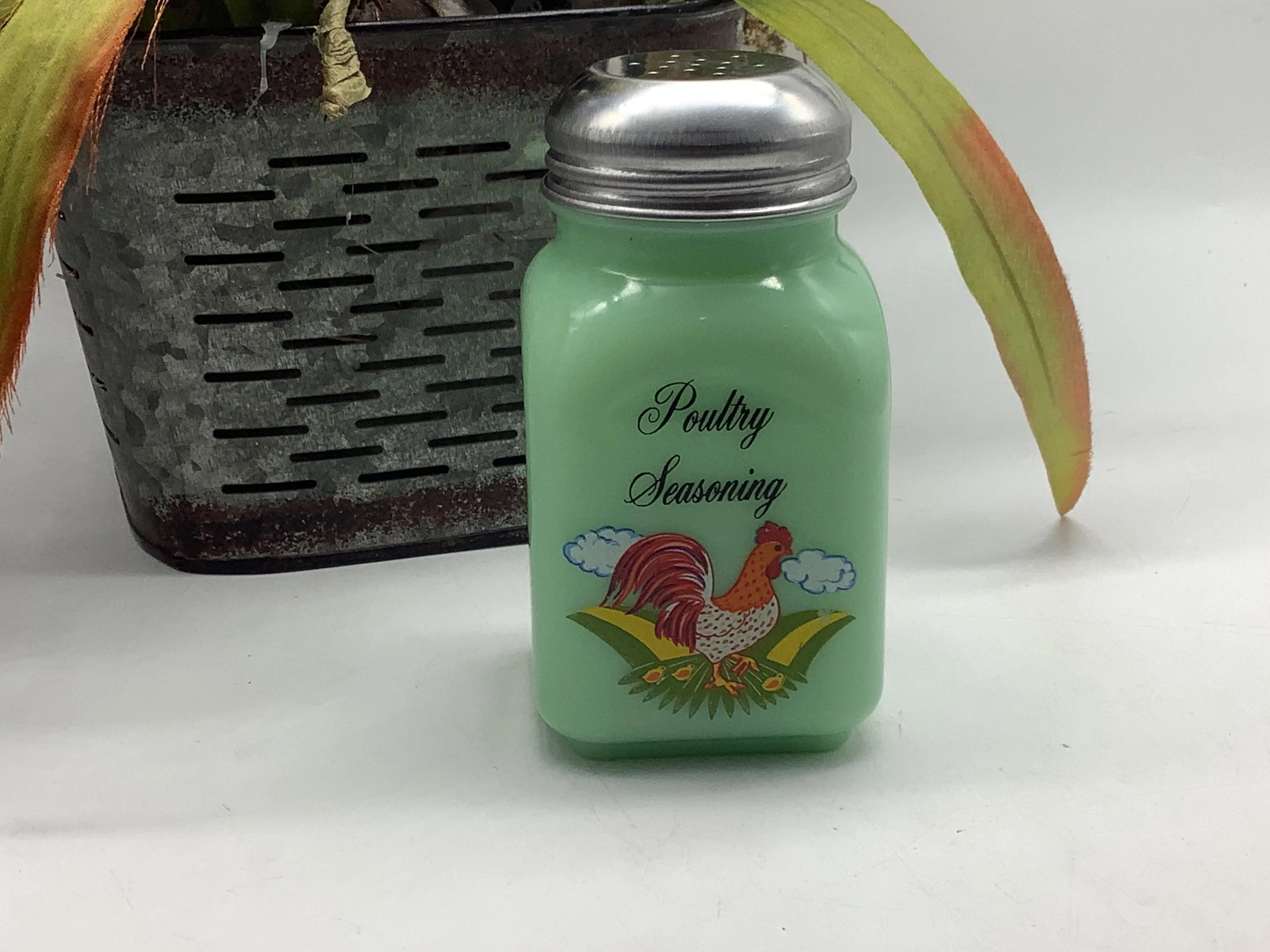 A small glass jar filled with homemade poultry seasoning on a kitchen counter with measuring spoons nearby