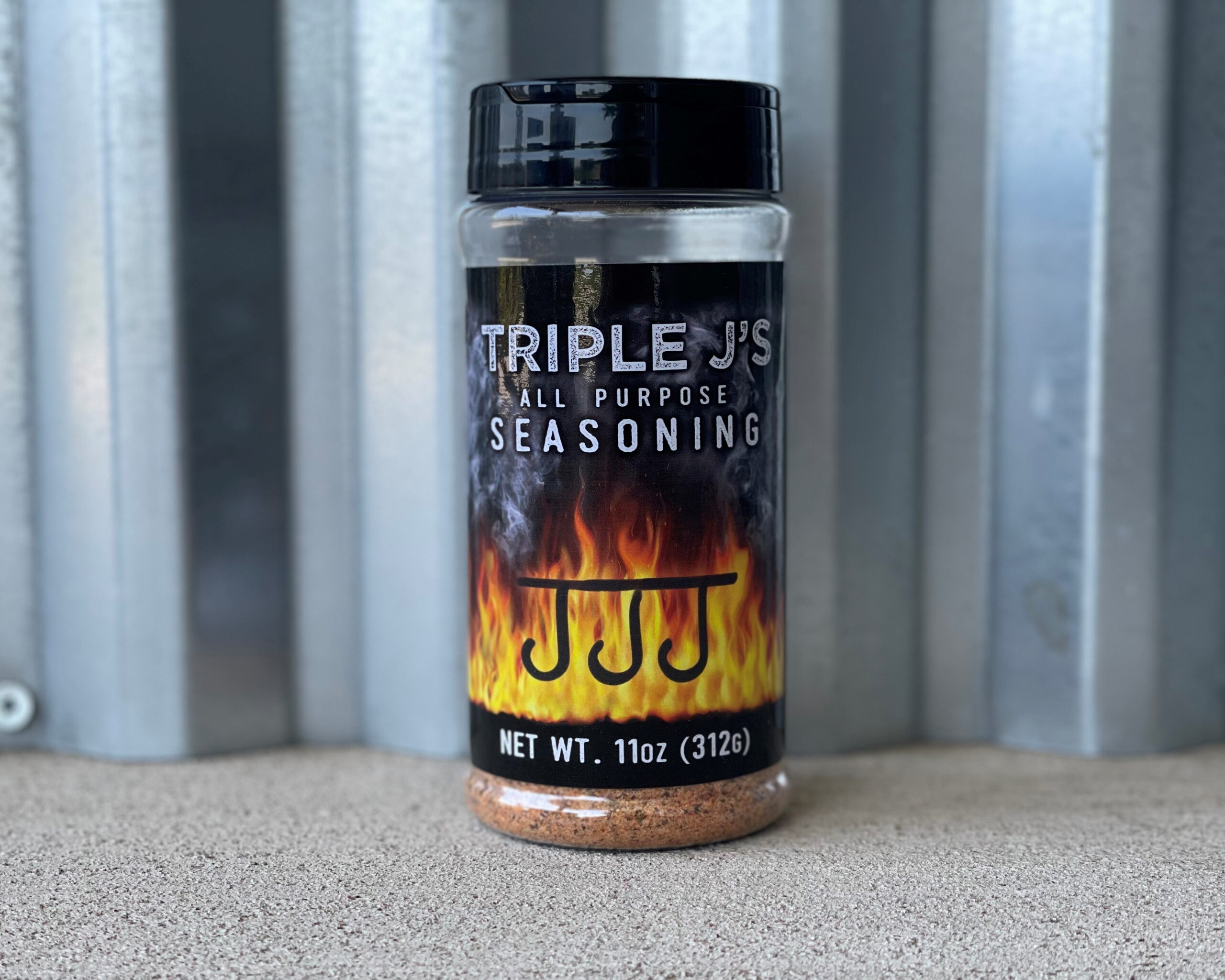 A small glass jar of homemade all-purpose seasoning on a warm kitchen counter beside measuring spoons, with garlic powder, paprika, and black pepper in small bowls nearby