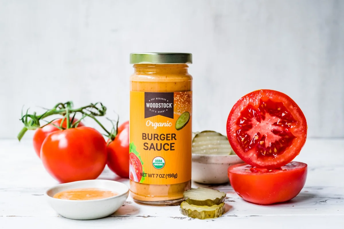 A small glass jar of homemade burger sauce with a lid on, sitting on a refrigerator shelf next to pickles and condiments