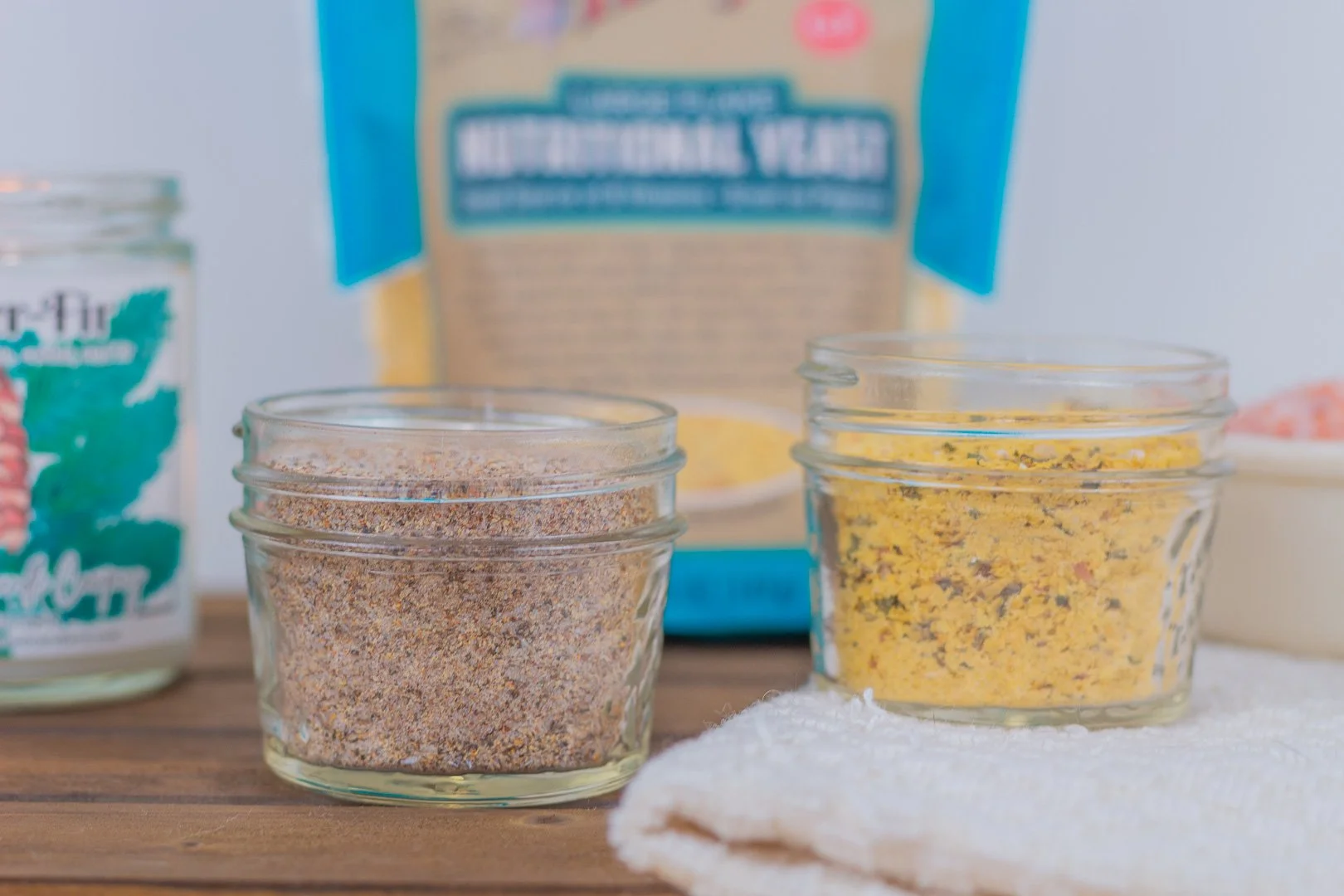 A small glass jar of homemade chicken seasoning with a measuring spoon on a warm kitchen counter, spices softly scattered nearby