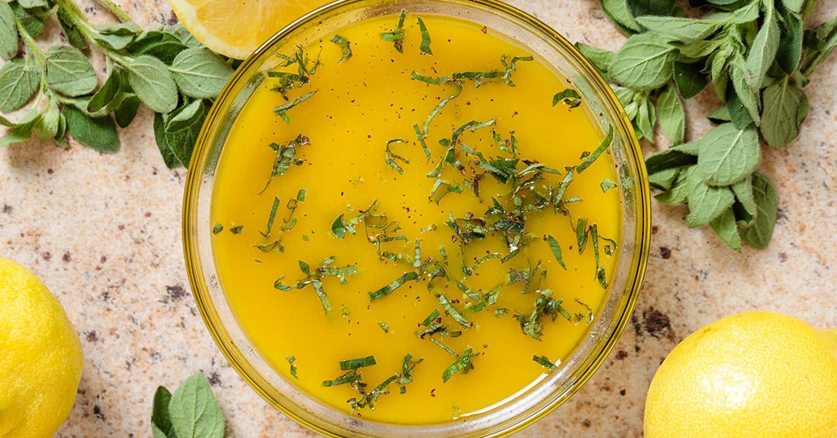 A small glass jar of lemon oregano vinaigrette with visible specks of oregano and minced garlic sitting on a kitchen counter