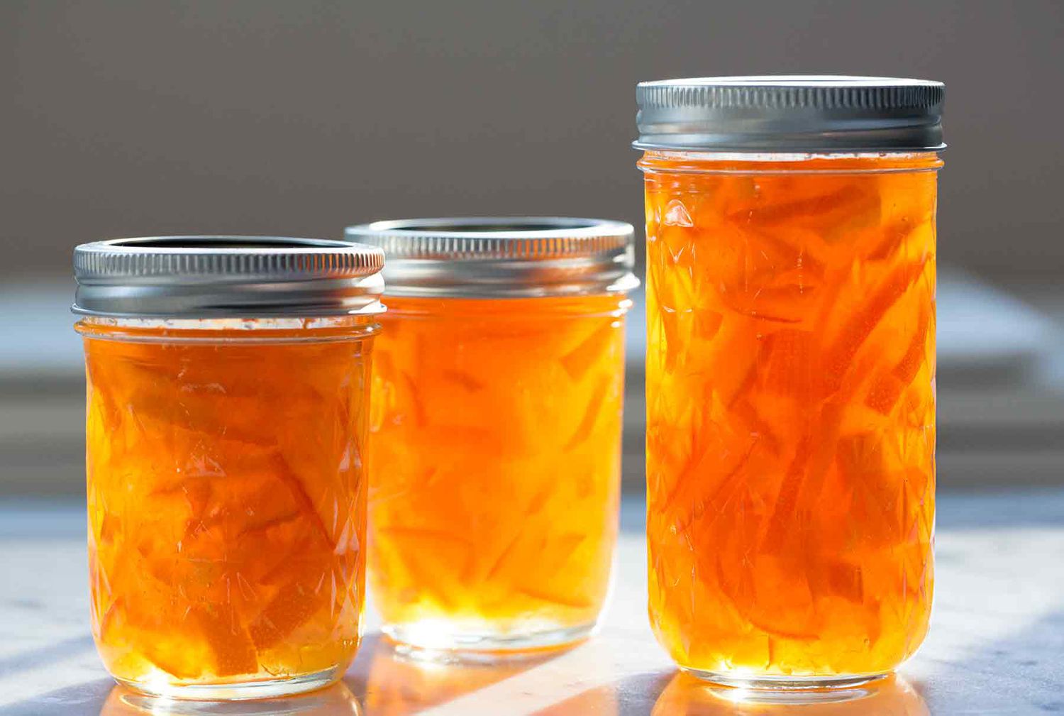 A small glass jar of orange peel marmalade with visible ribbons of peel beside a buttered slice of toast