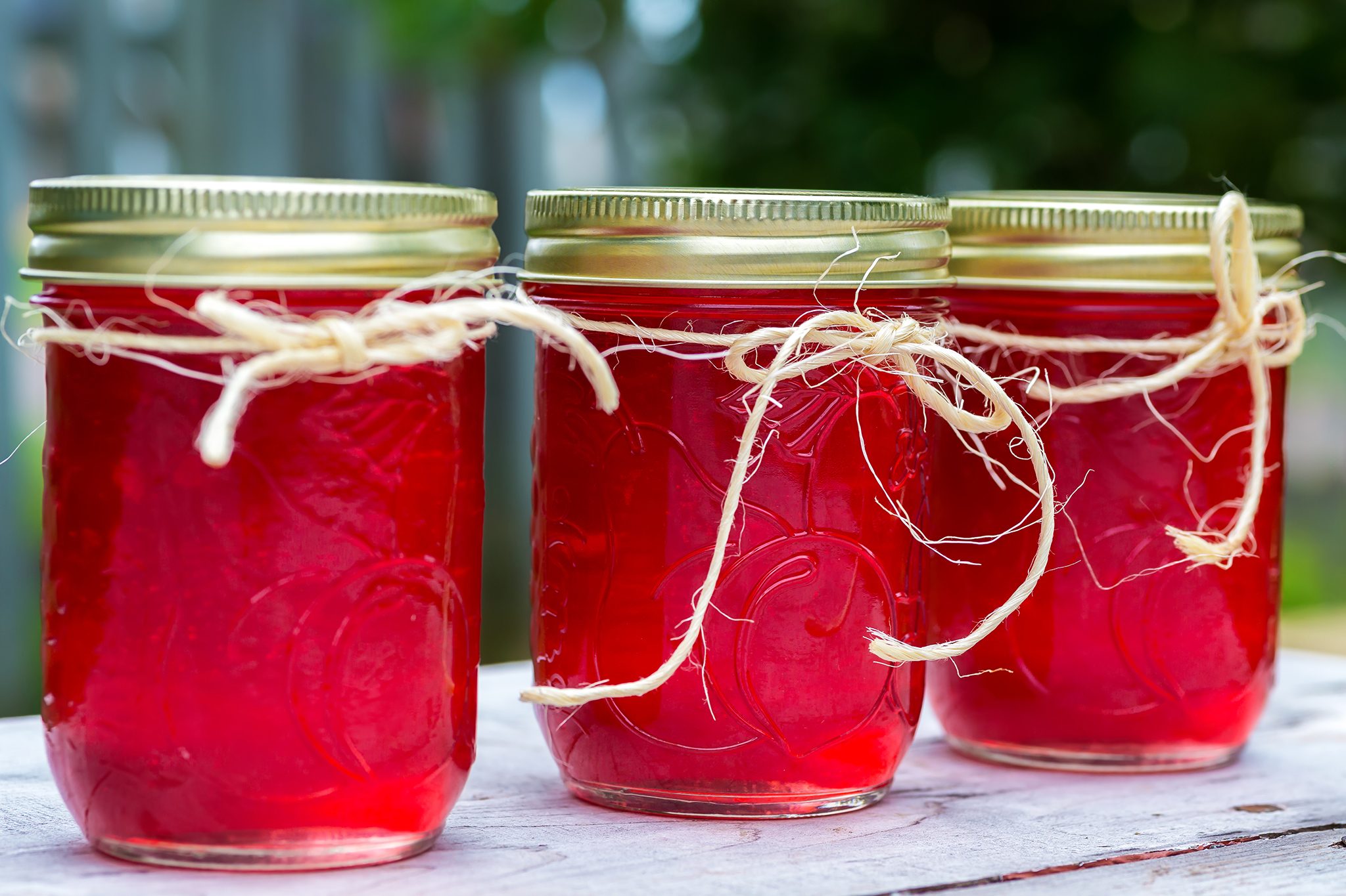 A small glass jar of ruby crab apple jelly on a wooden kitchen counter with a spoon and a few whole crab apples nearby, warm natural window light