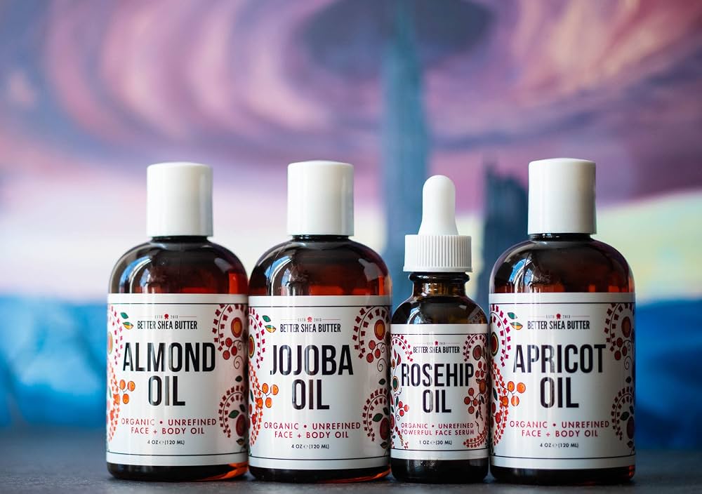 A small grouping of ingredients on a kitchen counter: a bowl of shea butter, a bottle of jojoba oil, a bottle of rosehip oil, and a small dish of beeswax pellets in warm natural light