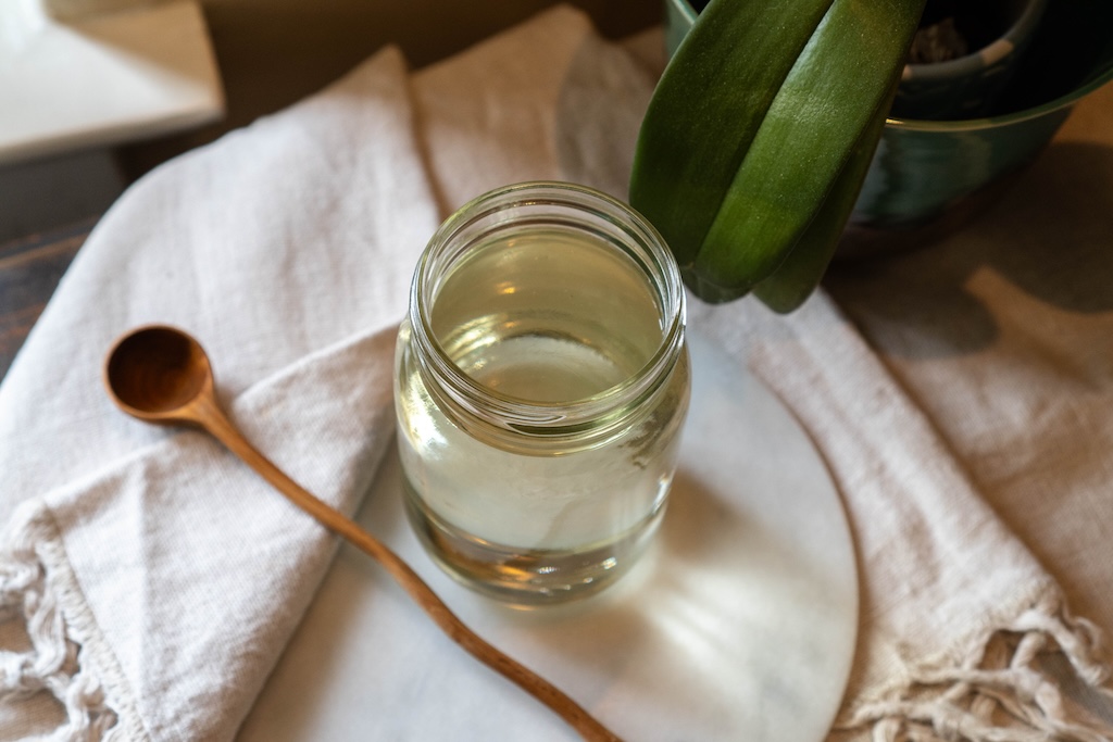 A small jar of simple syrup with a spoon beside it on a kitchen counter, ready for cocktails