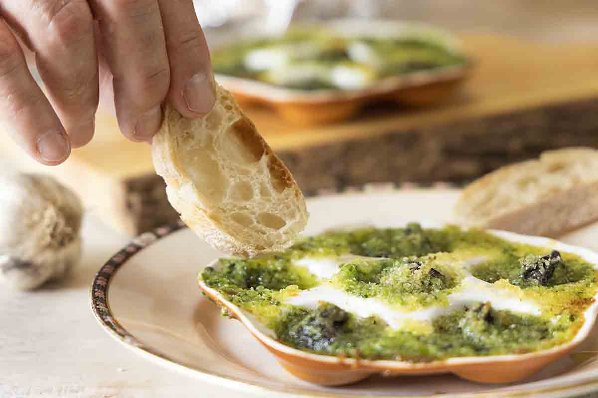 A small plate with a bubbling escargot dish and slices of baguette on a linen napkin at a softly lit dinner table