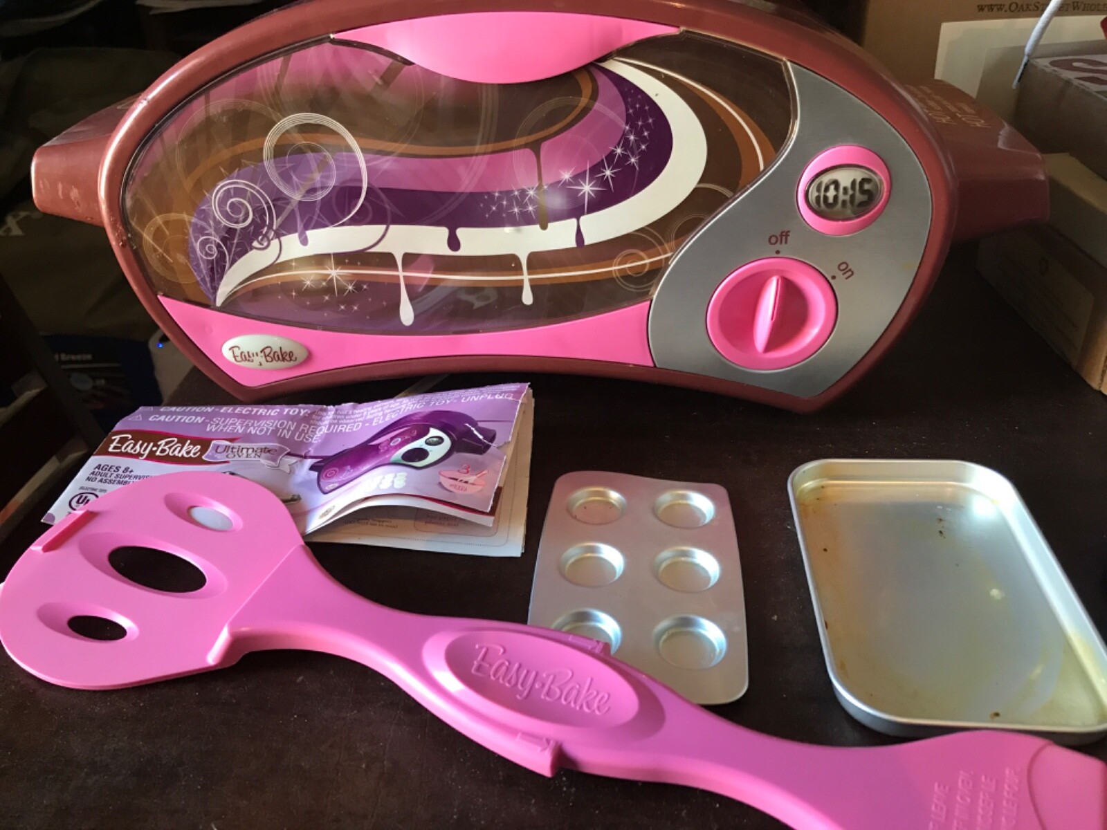 A small rectangular Easy-Bake style metal baking pan on a kitchen counter next to a spoon and a small mixing bowl