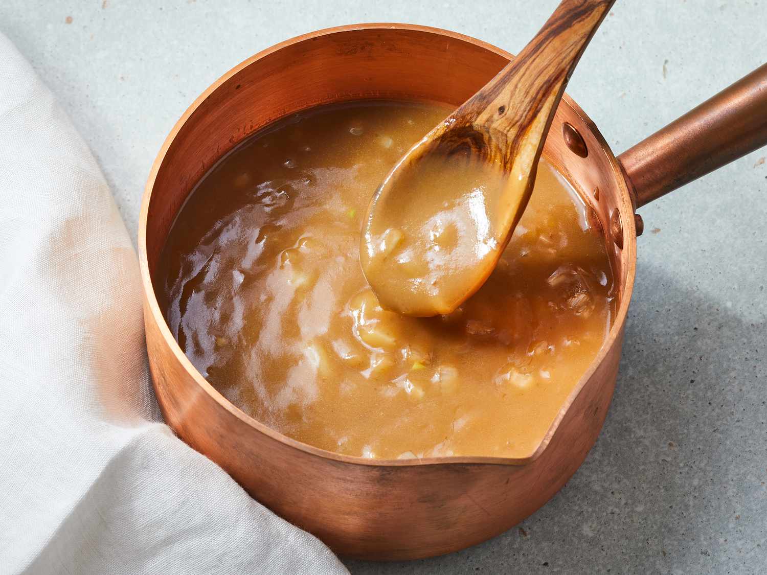 A small saucepan of brown gravy being whisked on a stovetop, with steam rising and a whisk resting in the pan