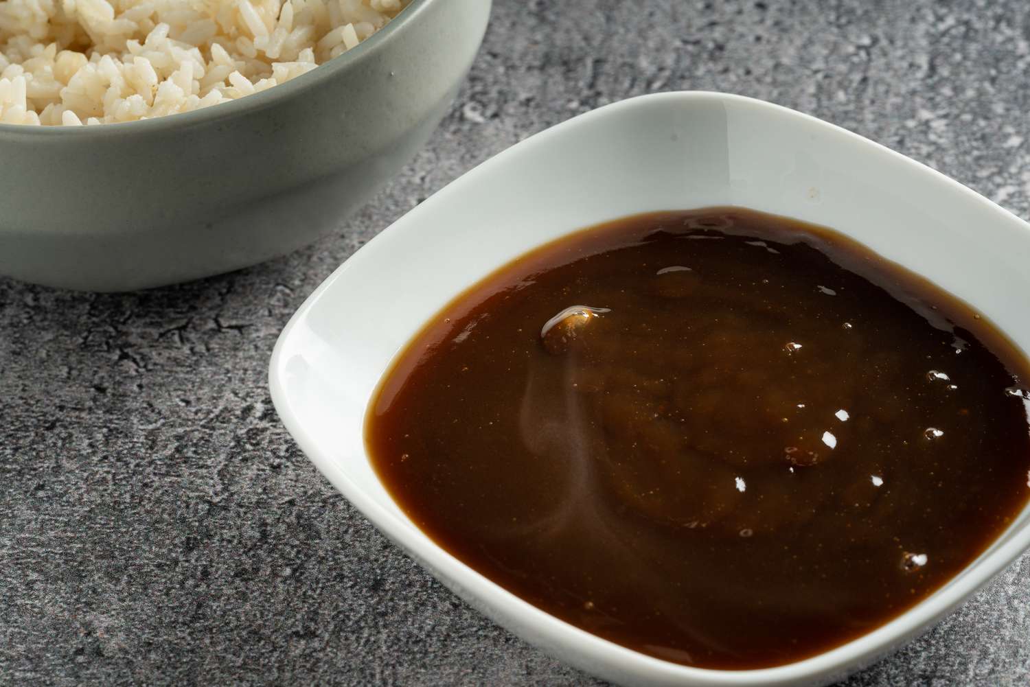 A small saucepan of glossy brown gravy on a stovetop with a whisk resting beside it