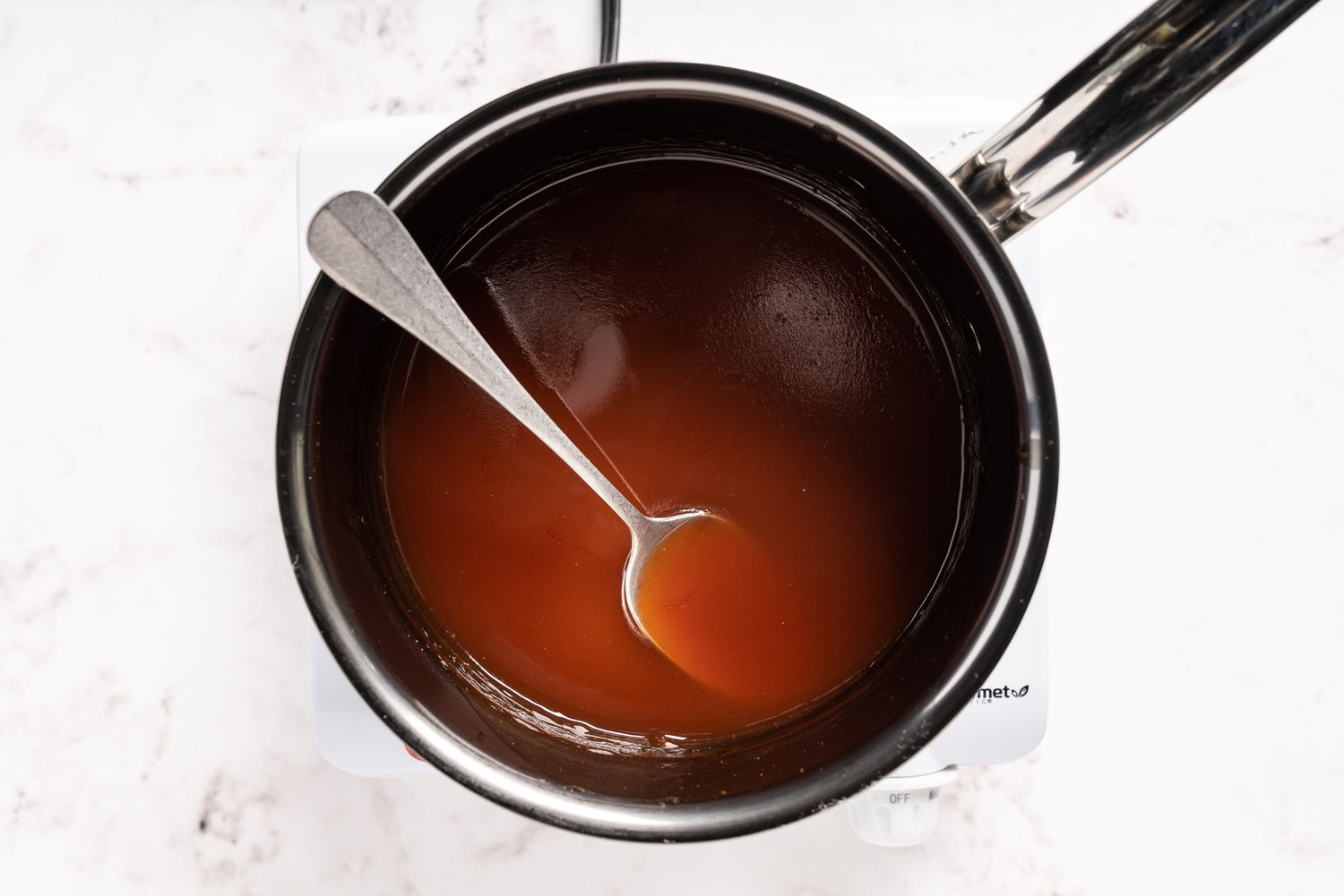 A small saucepan of glossy sweet and sour sauce being stirred with a wooden spoon on a home stove, warm kitchen lighting