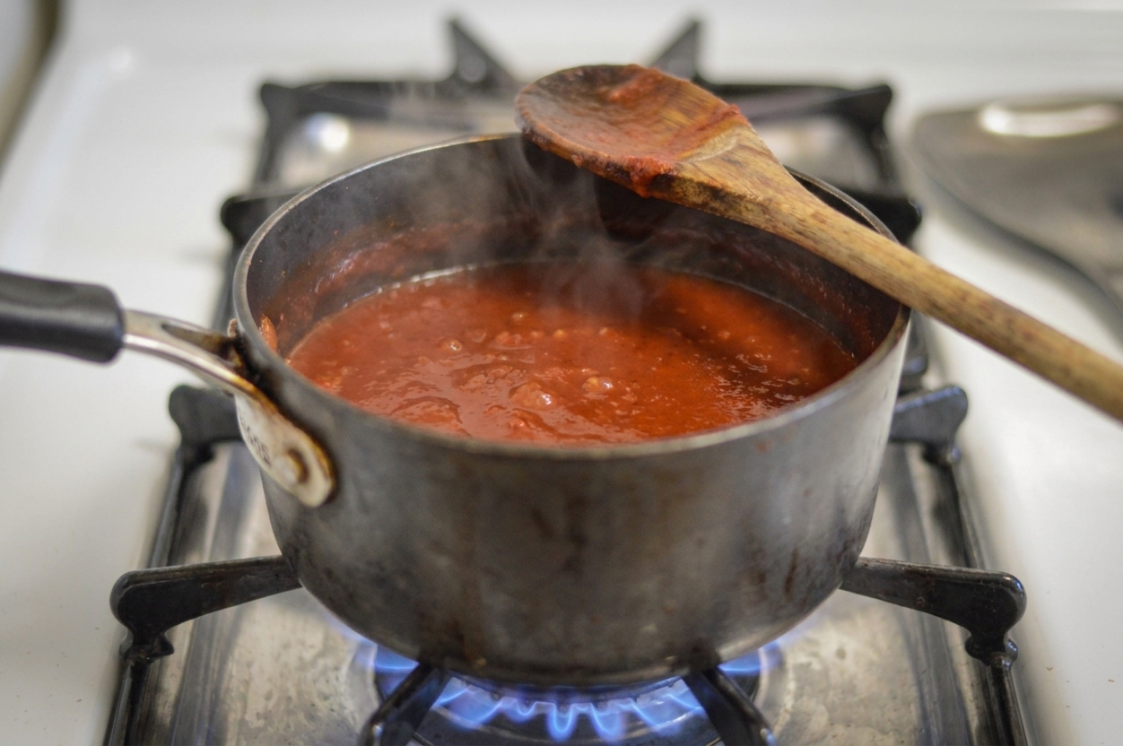 A small saucepan of smoky tomato sauce simmering on the stove with a wooden spoon resting on the rim