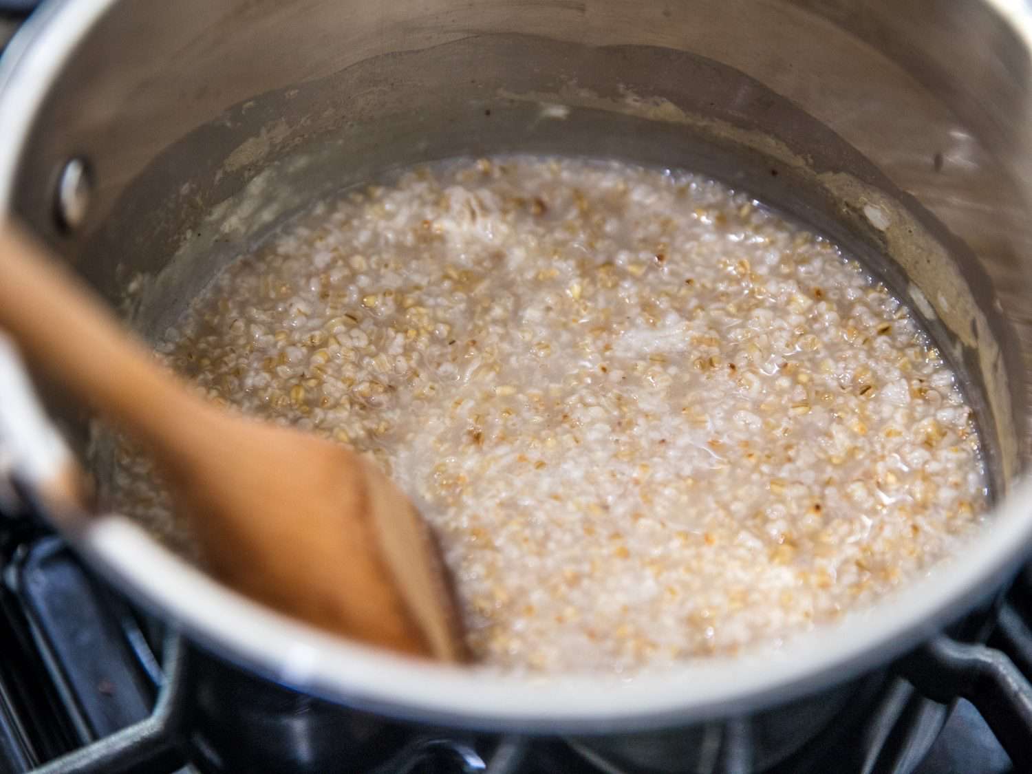 A small saucepan on a stove with leftover savory oatmeal being stirred with a wooden spoon while broth is poured in to loosen it