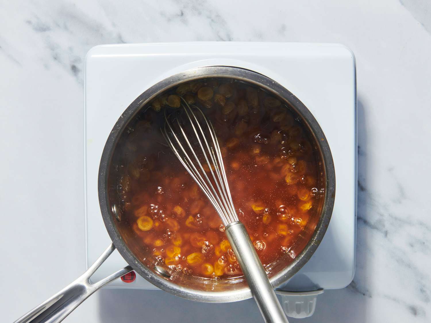 A small saucepan on a stovetop with brown sugar glaze being whisked until glossy