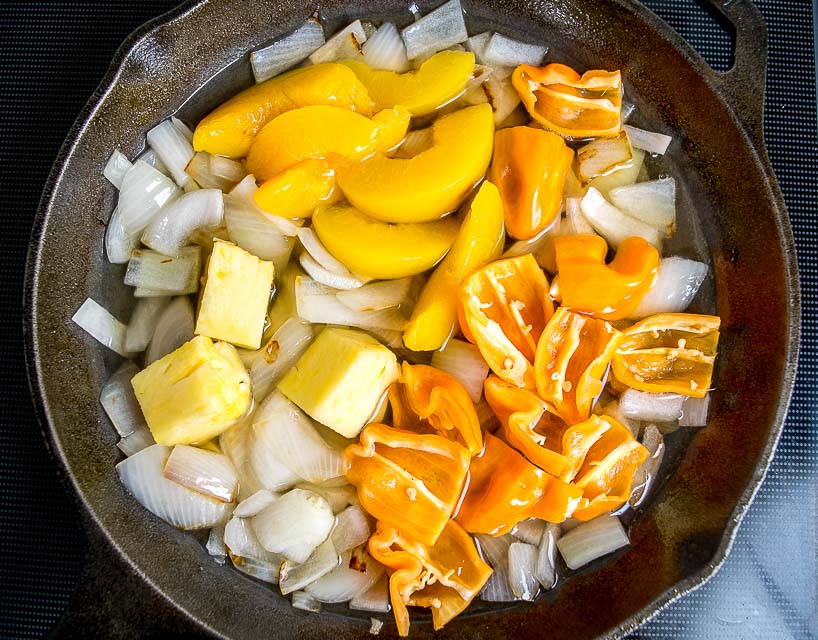 A small saucepan on a stovetop with habanero peppers, carrots, onions, and garlic gently simmering in a light orange vinegar broth, steam rising