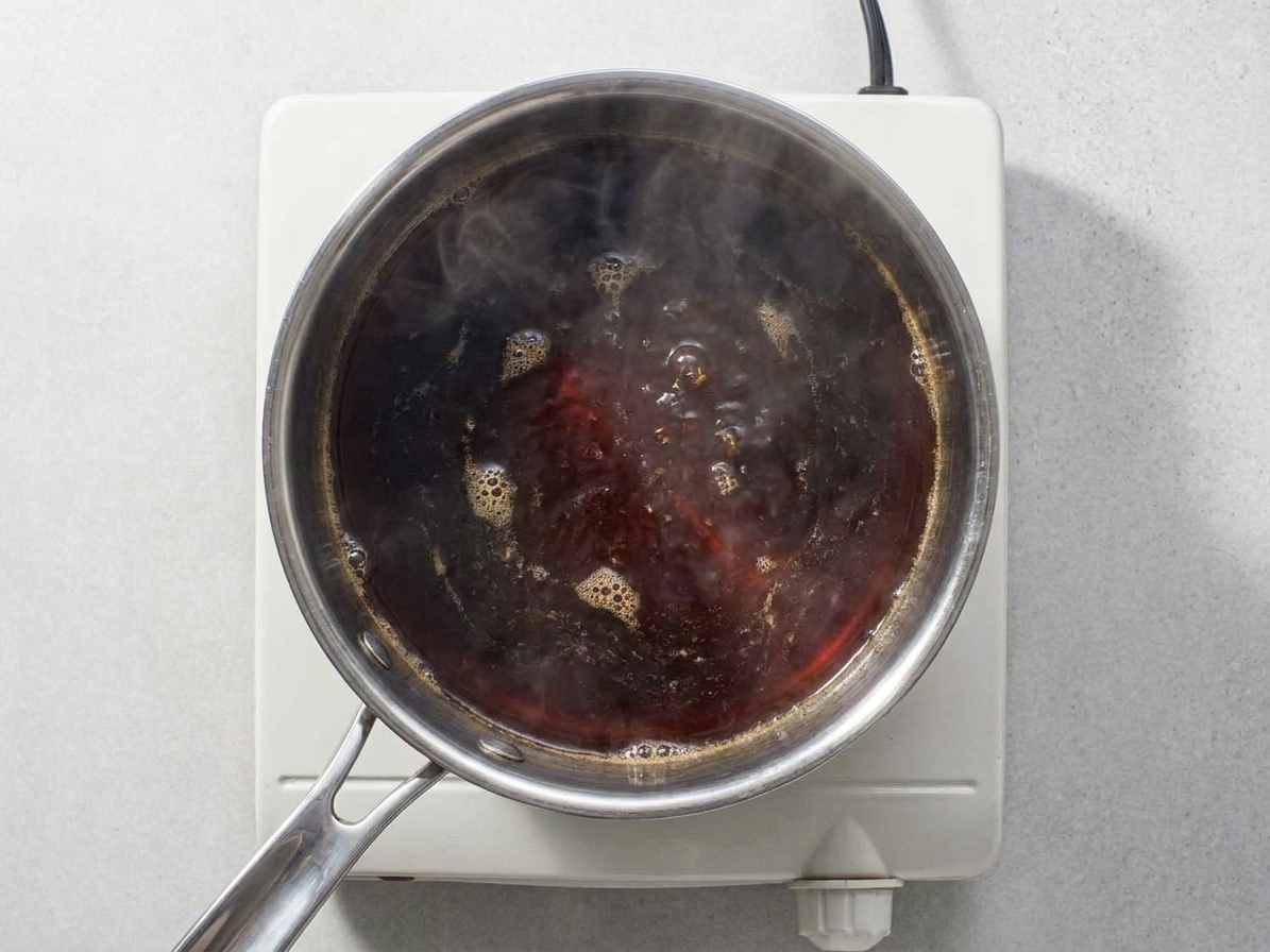 A small saucepan on the stove with shoyu tare gently simmering, steam rising