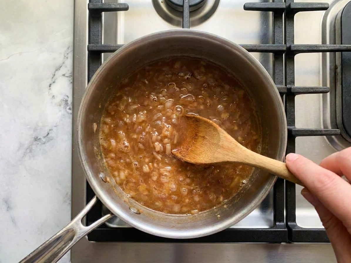 A small saucepan simmering apple cider sauce with shallots on a stovetop