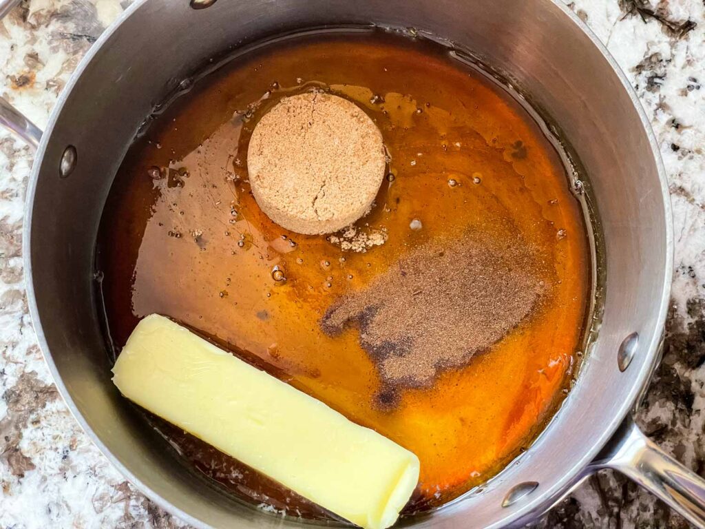 A small saucepan with melted butter and brown sugar being whisked into a glossy cinnamon syrup on a stovetop