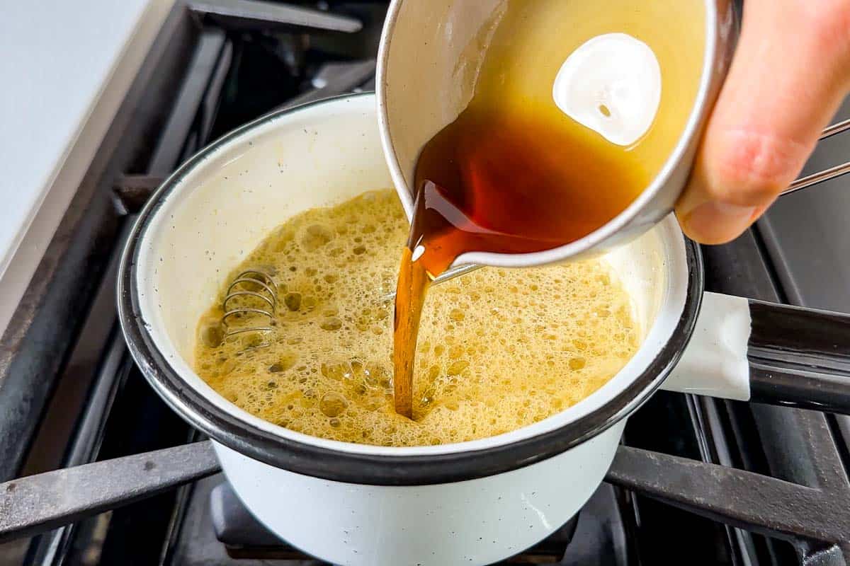 A small saucepan with melted butter and maple syrup being stirred with a spoon on a stovetop
