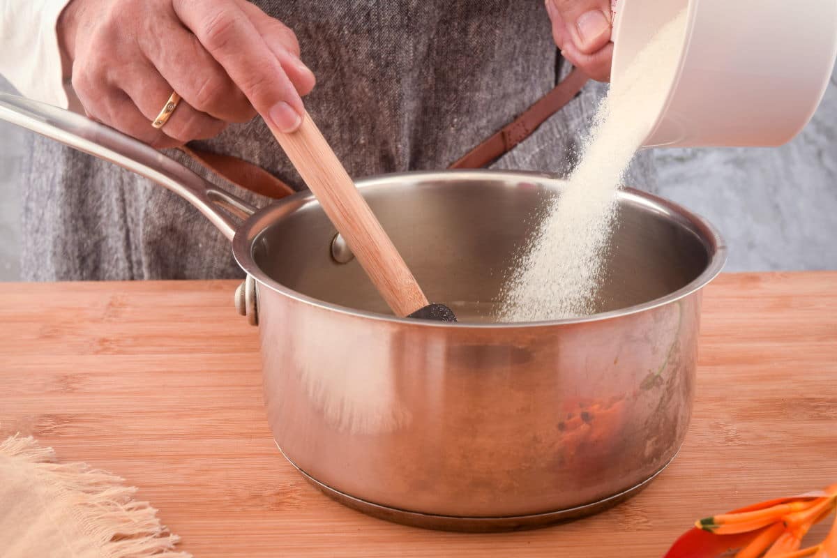 A small saucepan with sugar and water being stirred on a stovetop to make simple syrup