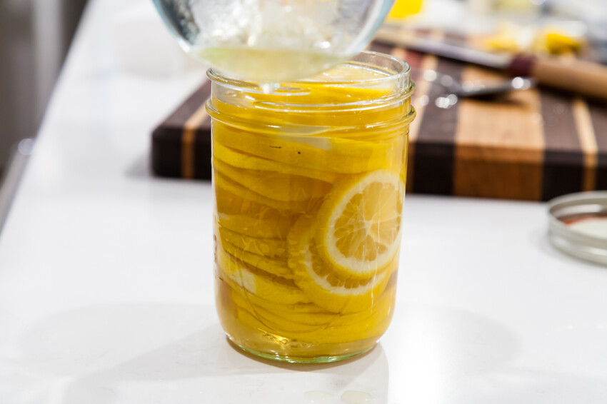 A small sealed jar of lemon base on a refrigerator shelf beside fresh lemons