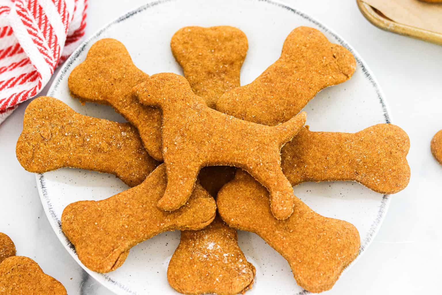 A small stack of bone-shaped peanut butter and pumpkin dog cookies on a parchment-lined baking sheet on a warm-toned kitchen counter