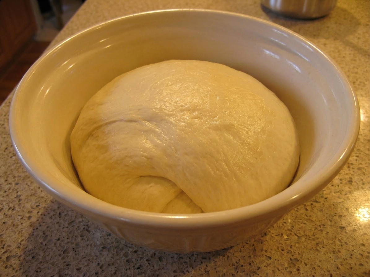 A smooth, elastic ball of bread dough resting in a mixing bowl after kneading