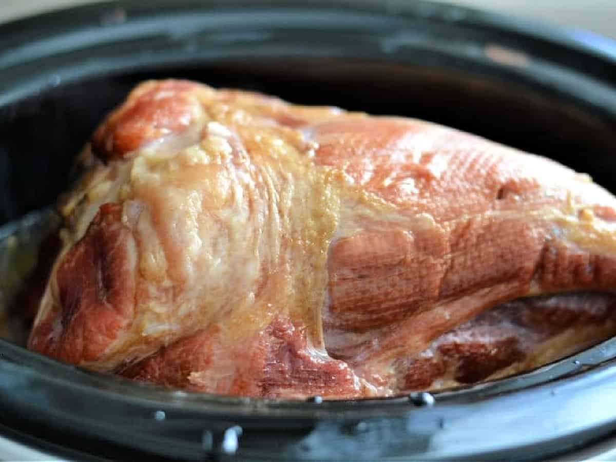 A spiral-cut ham placed inside a slow cooker insert on a kitchen counter before adding glaze