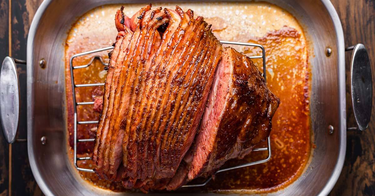 A spiral-cut ham sitting cut-side down in a roasting pan, with foil laid out ready to tent over the ham on a kitchen counter