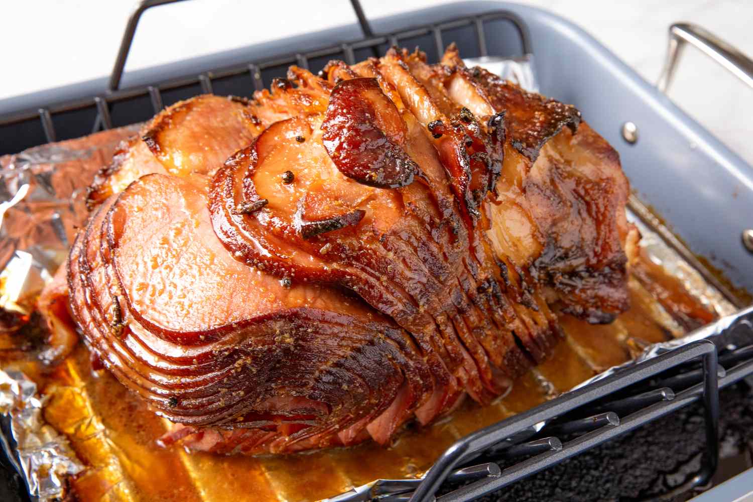 A spiral-sliced fully cooked ham sitting in a roasting pan lined with foil on a kitchen counter
