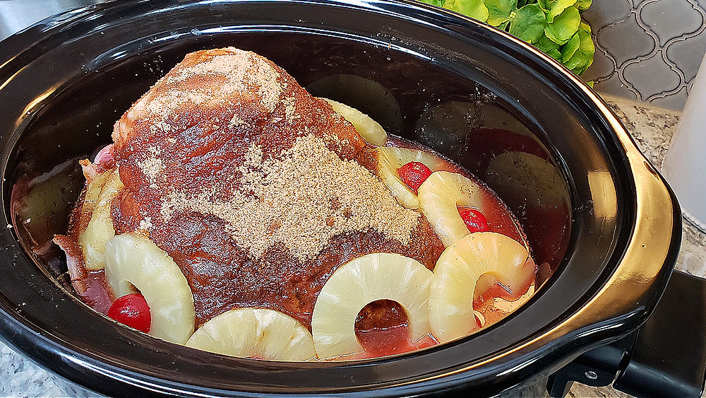 A spiral sliced ham in a slow cooker with glossy brown sugar pineapple glaze pooling around the edges on a warm kitchen counter