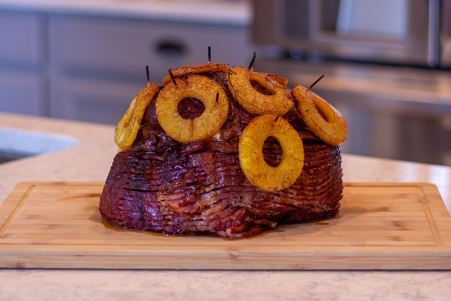 A spiral sliced ham on a serving platter with a shiny honey glaze, caramelized edges, and a small bowl of glaze on the side on a warm kitchen table