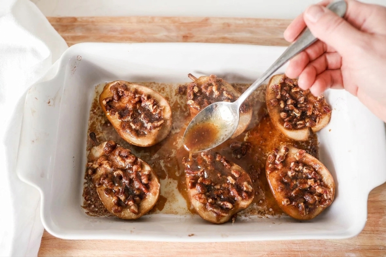 A spoon basting pear halves with brown sugar butter sauce in a baking dish