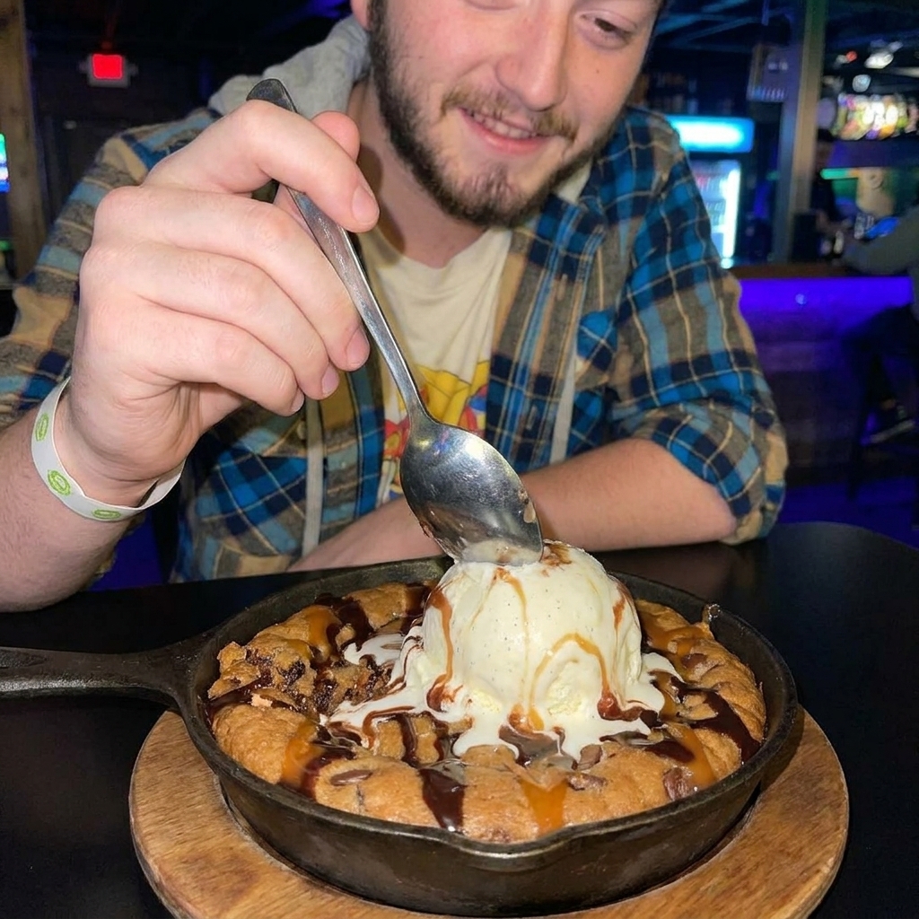 A spoon scooping a warm, gooey chocolate chip skillet cookie topped with a melting scoop of vanilla ice cream, close-up food photo